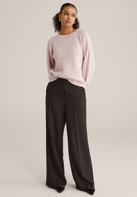 Világos rózsaszín kötött pulóver halszálka mintával, fekete, bő szárú nadrággal és hegyes orrú cipővel párosítva. Sima textúra, kényelmes szabás.