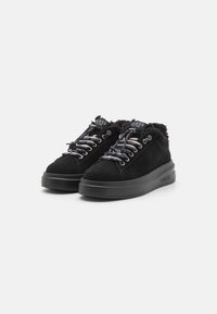 Sneakers in suede nera con un morbido bordo in pelliccia, dotati di lacci neri e argento, e una suola spessa nera con il logo "GUESS" sul lato.