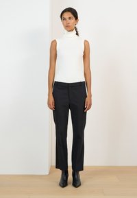 Biała bezrękawnikowa bluzka z golfem, zestawiona z czarnymi, dopasowanymi spodniami i czarnymi, szpiczastymi botkami za kostkę. Gładki materiał o dopasowanym kroju.