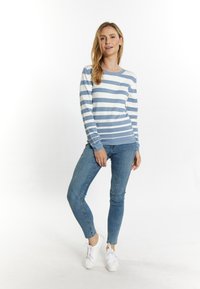 Pullover cu dungi albastre și albe, cu mâneci lungi, decolteu rotund și o formă ajustată, asortat cu blugi strâmți din denim și adidași albi.