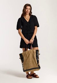 Fekete, rövid ujjú ruha húzózsinóros derékkal, hozzá nagy, juta anyagú, fekete díszítésű táska. A barna szandálok teszik teljessé az összeállítást.