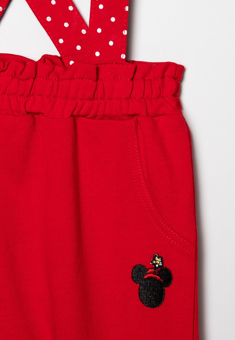 Rote Baumwoll-Latzhosen mit weißen gepunkteten Trägern, elastischem Bund und einem schwarzen gestickten Mickey-Maus-Akzent auf der Vordertasche.