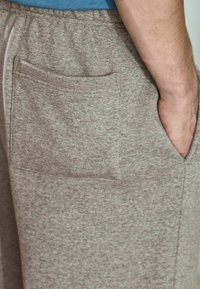 Szare dresy z miękkiego materiału, z tylną kieszenią. Tekstura jest lekko puszysta, z luźnym krojem i elastycznym pasem.