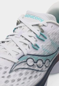 Λευκό και τιρκουάζ παπούτσι τρεξίματος Saucony με πλέγμα στον επάνω μέρος, λευκά κορδόνια και γεωμετρική λεπτομέρεια στην ενδιάμεση σολά.