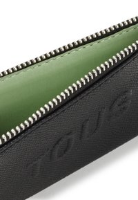Rifinitore nero in pelle con texture, con interno in tessuto verde, dotato di una cerniera argentata e marchiatura in rilievo sulla parte esterna.