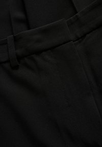 Črn oblečen material z gladko teksturo, ki ima raven pas in subtilne detajle šivanja. Brez vidnih vzorcev ali kovinskih delov.