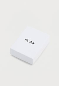 Λευκό ορθογώνιο κουτί με λεία υφή, που φέρει τη λέξη "PIECES" με παχύ μαύρο τύπο στο πάνω μέρος. Απλός σχεδιασμός, χωρίς μοτίβα ή διακοσμητικά στοιχεία.