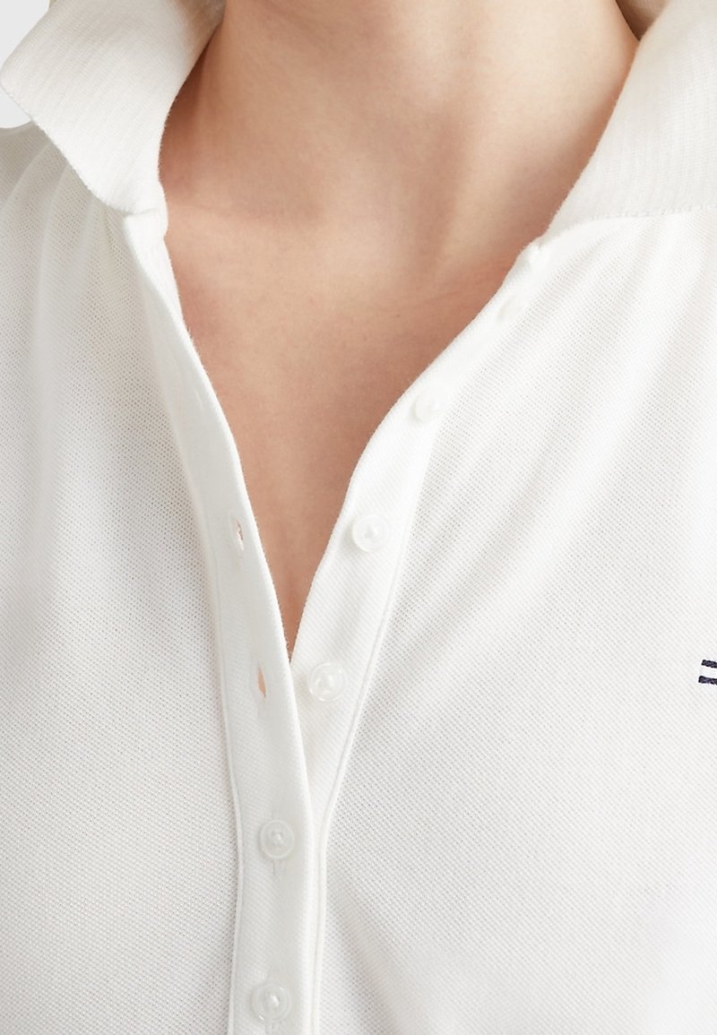 Gros plan d'une personne portant un polo blanc boutonné en tissu texturé avec un col partiellement ouvert.
