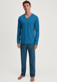 Ensemble de pyjama pour homme comprenant un haut bleu à manches longues et col en V avec une poche poitrine, associé à un pantalon de pyjama bleu à motifs géométriques.