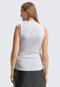 Mouwloze grijze top in een ribbeltextuur, met een hoge hals en een aansluitende silhouet, gecombineerd met een donkere, vloeiende rok.