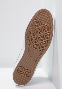 Suela de zapatilla de goma blanca con un patrón de agarre marrón texturizado, que presenta una forma de diamante y el logo "Converse All Star" en relieve.