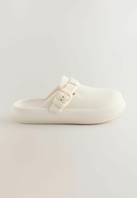 Witte rubberen klomp met een gestructureerd patroon, verstelbare band en stevige zool. Ronde neus en gesloten achterkant voor extra ondersteuning.