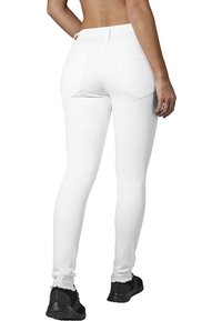 Jeans blancos ajustados con una textura suave, que presentan dos bolsillos traseros y una cintura alta, combinados con zapatillas deportivas negras.
