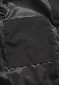 Doublure intérieure d’une veste noire avec une poche intérieure rectangulaire cousue sur un tissu satin lisse.