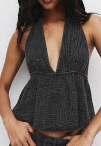 Haut halter noir texturé avec un décolleté en V profond, présentant une taille froncée et une silhouette fluide. Le matériau présente un motif légèrement froissé.