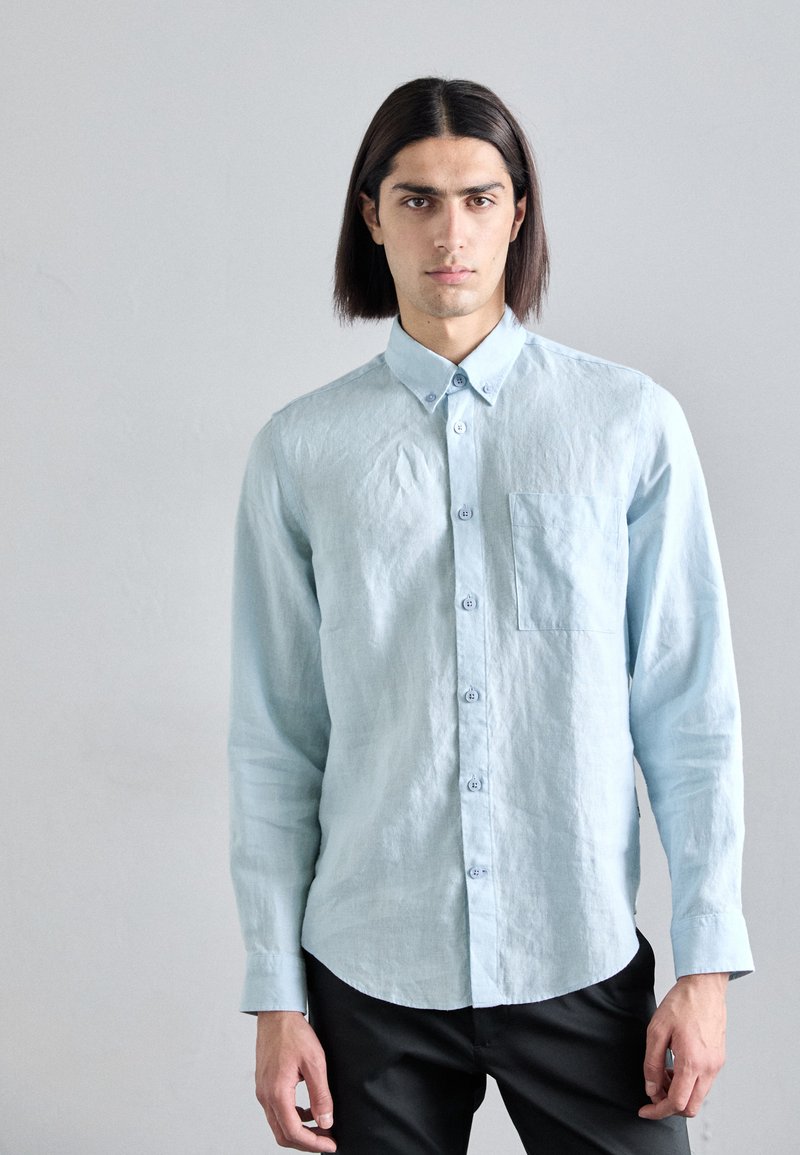 Camicia azzurro chiaro a maniche lunghe con bottoni, realizzata in tessuto testurizzato, dotata di una tasca sul petto e colletto con bottoni, abbinata a pantaloni neri.