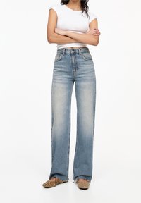 Jeans de pierna ancha en azul claro con una cintura alta, que cuentan con el clásico estilo de cinco bolsillos y un lavado desgastado para un look casual.