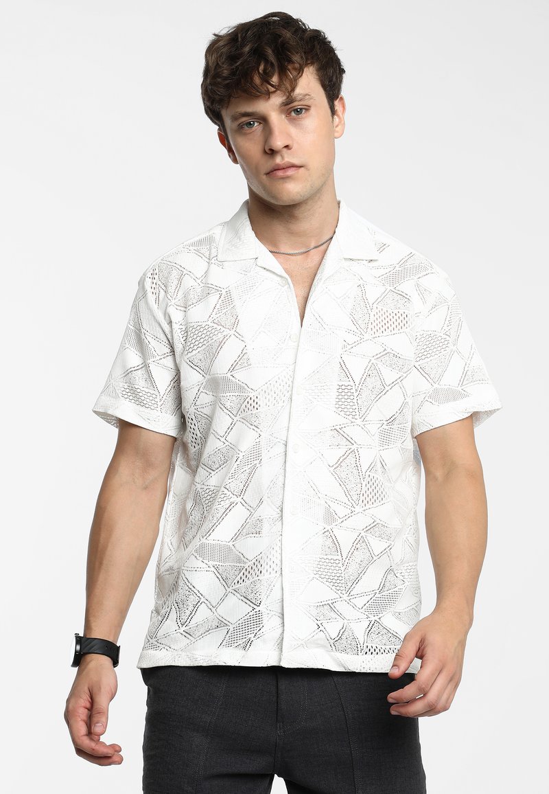 Korte mouwen witte shirt met een geometrisch uitgesneden patroon en een kraag. Draagt met grijze broek, die een lichtgewicht, gestructureerd ontwerp toont.