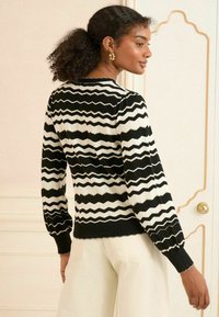 Sweter w czarno-białą zygzakowatą strukturę z długimi bufiastymi rękawami i ribbowanym wykończeniem. Tył ma teksturowany wzór z okrągłym dekoltem.