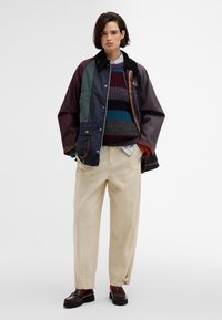 Többszínű dzseki fekete gallérral, csíkos pulóver, krémszínű nadrág és sötét mokaszin. Különböző textúrák és merész színek jellemzik.