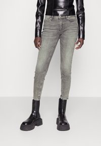 Jeans de mezclilla gris de corte slim-fit con un lavado desgastado, diseño de cinco bolsillos y detalles metálicos, combinados con botas negras de tobillo gruesas.
