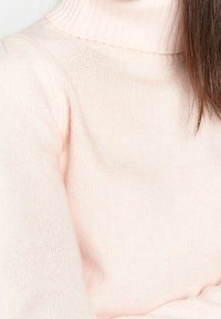 Pull turtleneck tricoté rose clair avec un col côtelé et une texture douce, présentant un gros plan du tissu et des détails de couture.