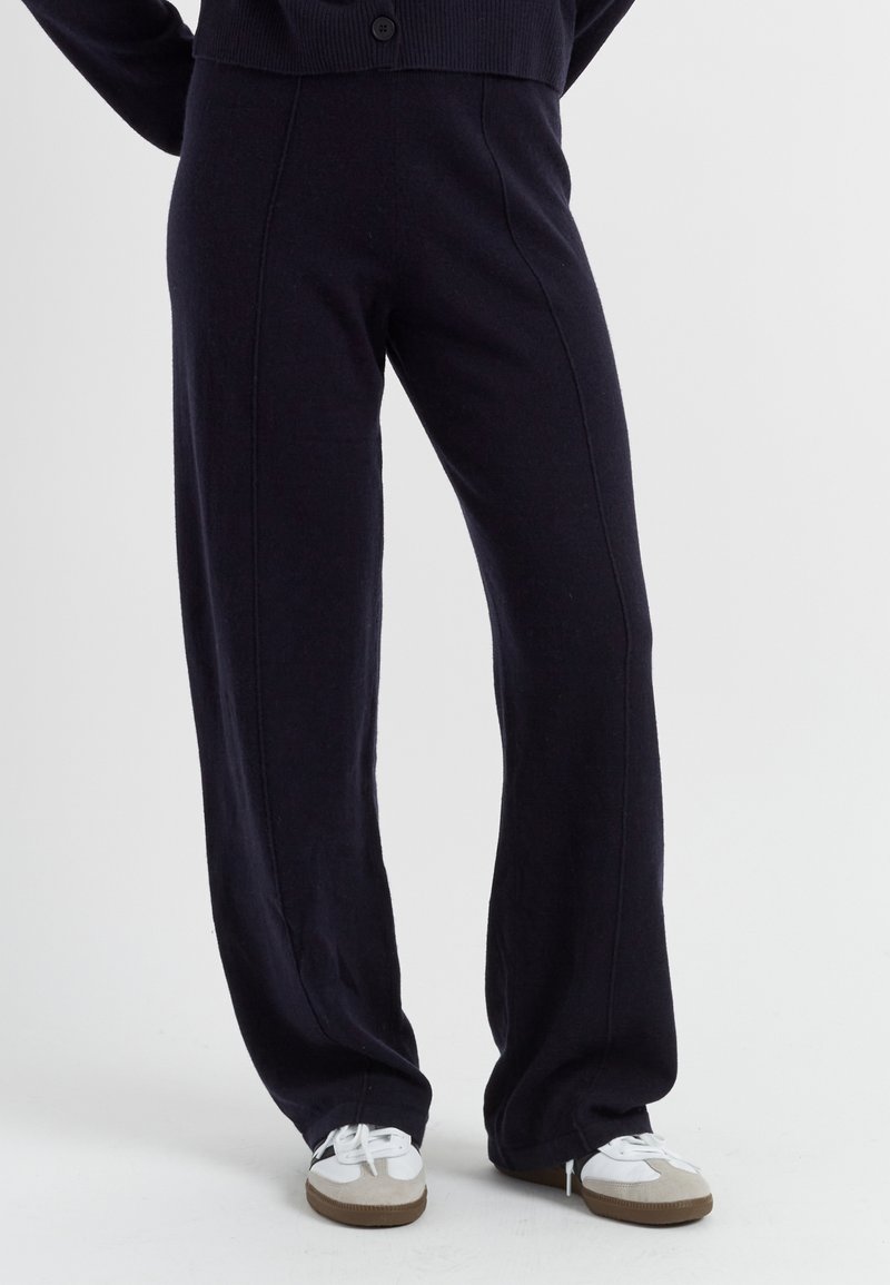 Navyblauwe wijde broek gemaakt van zacht materiaal, met een getextureerde afwerking en zichtbare naden. Gepaard met witte en grijze sneakers.