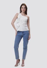 Hvid én-skulder top med flæsedetalje; blå jeans med lodrette hvide striber; sølv hæle sandaler; minimalistisk design.