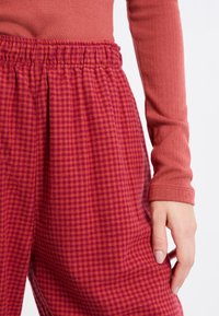 Czerwono-pomarańczowe spodnie w kratę z elastycznym pasem, w zestawie z dopasowanym topem z długim rękawem w uzupełniającym jednolitym kolorze.