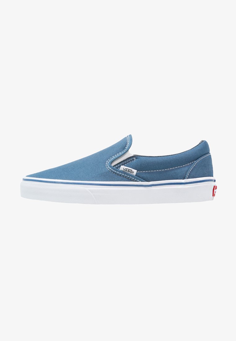 Zapatilla azul de lona sin cordones con suela de goma blanca, lados elásticos, acentos de costura blanca y una etiqueta roja con el logo en el talón.