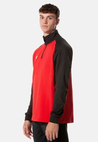 Rot schwarz gefütterter Pullover mit Reißverschluss am Hals, langen Ärmeln, entspannter Passform und weichem Stoff, mit einem Logo auf der Brust.