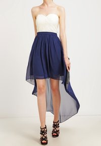 Sukienka bez ramion z plisowanym ivoire gorsetem i zwiewnym granatowym dołem w stylu high-low. Noszona z czarnymi sandałkami na szpilce i kopertówką.