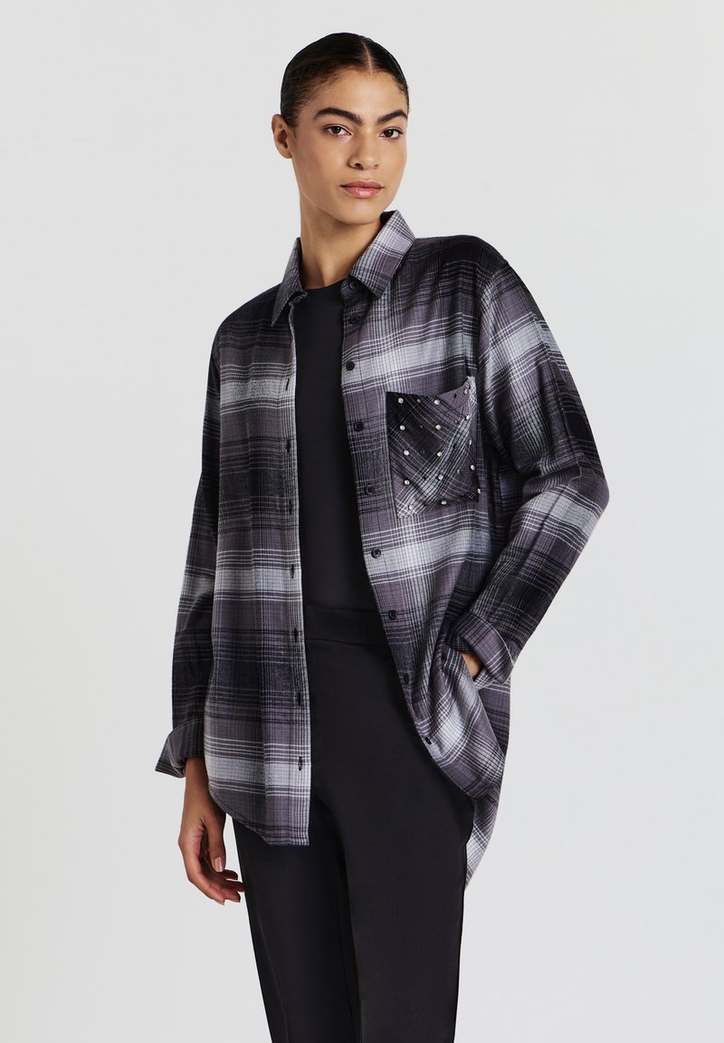 Kariertes Flanellhemd in Grau und Schwarz, mit einer Tasche mit metallischen Nieten, durchgehender Knopfleiste und lockerem Schnitt. Glatte Textur.