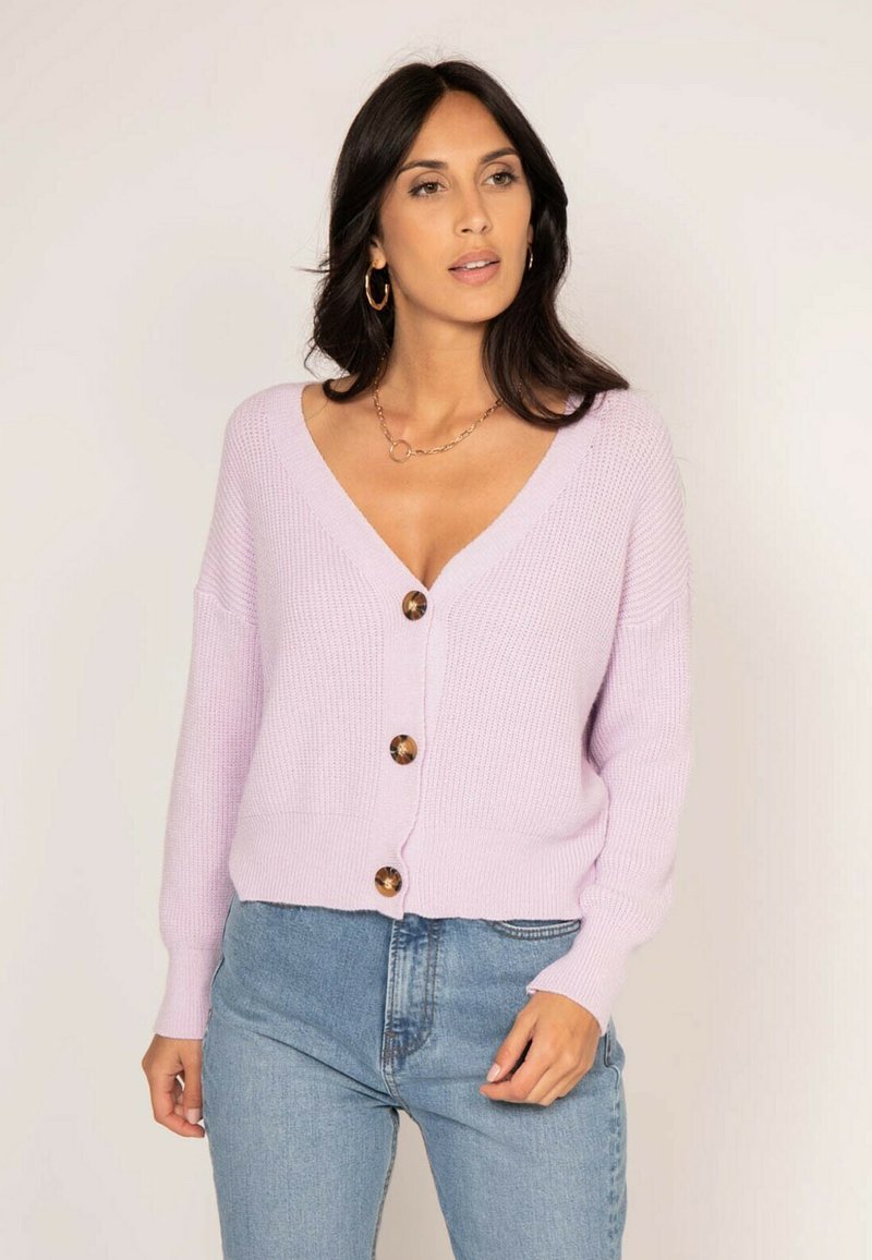 Cardigan tricoté lilas clair avec un décolleté en V profond, des manches longues et quatre boutons ronds marron sur le devant. Texture douce, coupe courte.