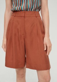 Bruine geplooide shorts gemaakt van een lichtgewicht stof. Heeft een hoge taille en een rechte, relaxte pasvorm met omgeslagen zomen aan de onderkant.