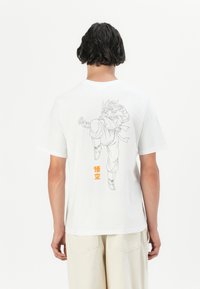 Bílá bavlněná trička s šedým liniovým nákresem postavy v kick póze na zadní straně, se oranžovým japonským textem pod obrázkem.