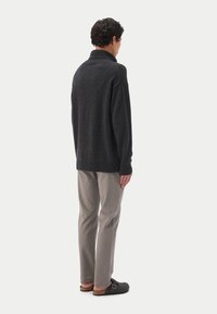 Dunkelgrauer Strickpullover mit hohem Kragen, kombiniert mit hellgrauen Hosen und dunklen Hausschuhen, in lockerer Passform mit gerippten Bündchen.