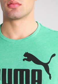 Grön bomullströja med rund halsringning, med en stor svart Puma-logotyp och fet "PUMA" text i kontrasterande svart under.