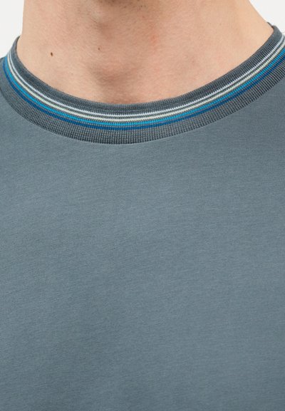 Κοντινό πλάνο στο λαιμό και το άνω μέρος του στήθους ενός ατόμου που φοράει γκρι πουκάμισο με στρογγυλή λαιμόκοψη ριγέ σε μπλε, λευκό και γκρι χρώμα.