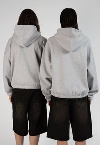 Sweatshirts à capuche gris avec un ourlet élastique, portés sur un short en denim noir. Les sweatshirts ont une coupe décontractée et une poche kangourou.
