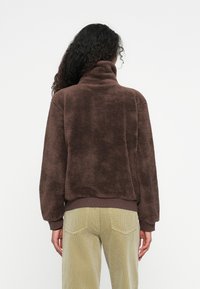 Bruine, fuzzy fleece pullover met een hoge kraag en geribbelde zoom, gecombineerd met lichtgroene ribfluwelen broek. Gelaagd, ontspannen pasvorm ontwerp.