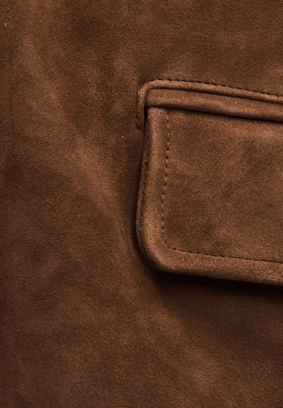 Καφέ ύφασμα από σουέντ με ραμμένη ορθογώνια πτερυγιοθήκη τσέπης με στρογγυλεμένες γωνίες και διακόσμηση ραφής σε τόνους ίδιους με το ύφασμα.
