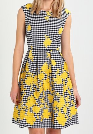 Bezrekawowa sukienka w czarno-białą kratę z jasnymi żółtymi wzorami kwiatowymi, dopasowaną talią i plisowanym dołem.