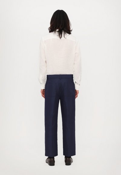 Fehér len hosszú ujjú ing, gombos mandzsettával, tengerészkék, széles szárú nadrággal párosítva, két hátsó zsebbel. Egyszerű dizájn, puha tapintás.