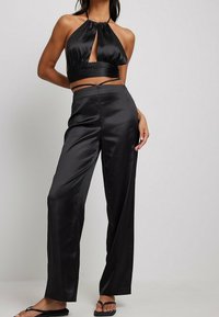 Ensemble deux pièces en satin noir comprenant un crop top à col halter avec une découpe en trou de serrure et un pantalon large taille haute. Texture lisse tout au long.