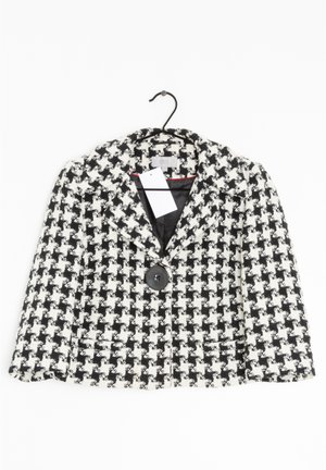 Zwart-wit blazer met houndstooth-patroon, één grote knoop en voorzakken, tentoongesteld aan een zwarte hanger met een wit label.
