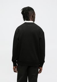 Sudadera negra con puños y dobladillo acanalados, con un logo sutil en la parte trasera. El diseño es de corte holgado, fabricado con material de algodón suave.