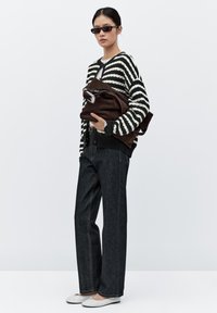 Pruhovaný černobílý svetr, tmavé džíny rovného střihu, šedé baleríny, držící hnědou semišovou tašku se stříbrným zipem.