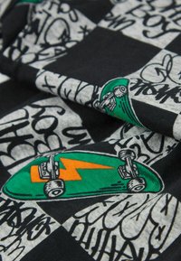 Bavlněná tkanina s kostkovaným vzorem v šedé a černé barvě, s grafickými prvky skateboardu ve stylu kreslených postaviček v zelené barvě a abstraktním černým graffiti textem.