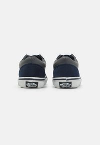Zapatillas bajas de ante azul marino y cuero gris con suelas de goma blanca. Presentan un logo "Vans Off the Wall" en el talón.